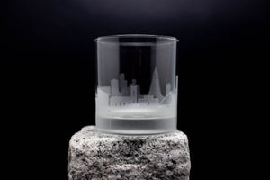 A frosted glass with an etched cityscape design on it, placed on a rock.