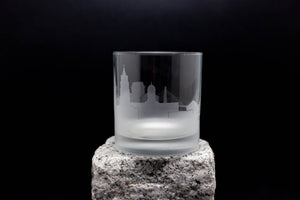 A frosted glass with a city skyline etched onto it, placed on a rock.
