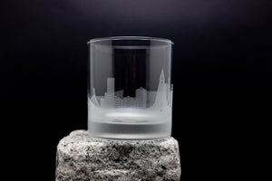 A frosted glass with a city skyline etched onto it, placed on a rock.