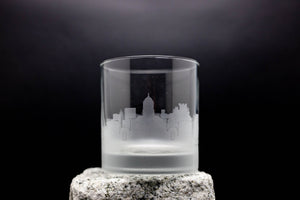A frosted glass with a city skyline etched onto it, placed on a rock.
