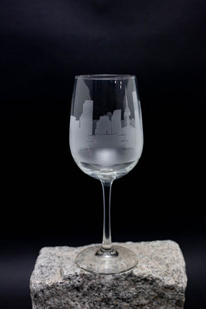 A wine glass with an etched cityscape design on it, placed on a rock against a dark background.