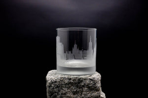 A frosted glass with a city skyline etched onto it, placed on a rock against a dark background.
