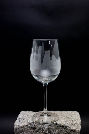 A wine glass with an etched city skyline design on it, placed on a rock against a dark background.