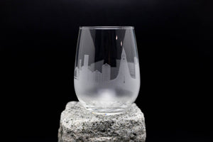A wine glass with an etched city skyline design on it, placed on a rock.