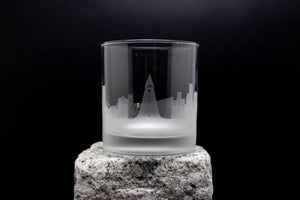 A frosted glass with an etched cityscape design on it, placed on a rock.