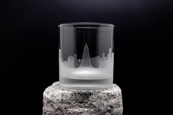 A frosted glass with an etched cityscape design on it, placed on a rock.