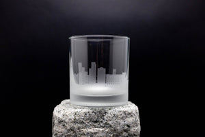 A frosted glass with a city skyline etched onto it, placed on a rock.