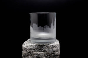 A frosted glass with a city skyline etched onto it, placed on a rock.