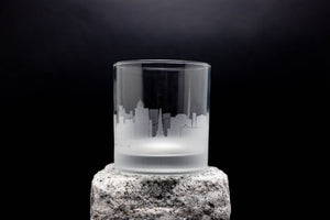 A frosted glass with a city skyline etched onto it, placed on a rock.