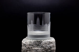 A frosted glass with an etched image of a city skyline on it, placed on a rock.
