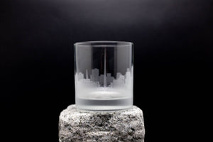 A frosted glass with a city skyline etched onto it, placed on a rock.
