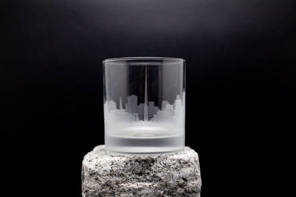 A frosted glass with a city skyline etched onto it, placed on a rock.