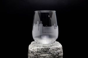 A wine glass with an etched city skyline design on it, placed on a rock.