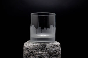 A frosted glass with a city skyline etched onto it, placed on a rock.