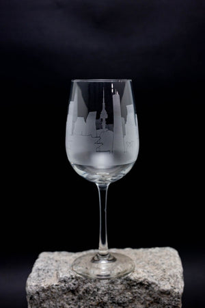 A wine glass with an etched cityscape design on it, placed on a rock.