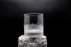 A frosted glass with a city skyline etched onto it, placed on a rock.