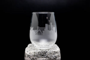 A clear glass with an etched image of a city skyline on it, placed on a rock against a black background.