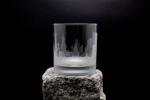 A frosted glass with a city skyline etched on it, placed on a rock against a dark background.