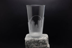 A clear glass with a city skyline printed on it, placed on a rock against a dark background.