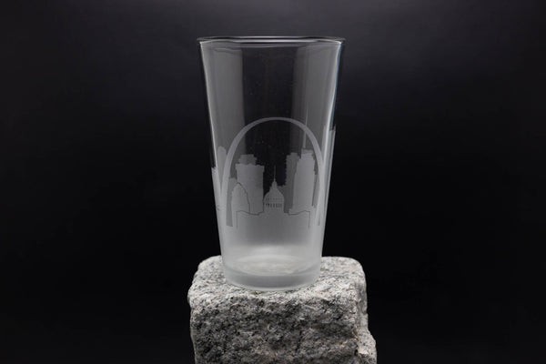 A clear glass with a city skyline printed on it, placed on a rock against a dark background.
