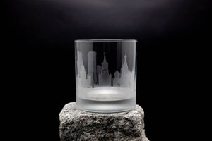 A frosted glass with a city skyline etched onto it, placed on a rock against a dark background.