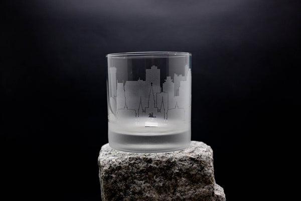 a glass on a rock with a city skyline etched on it