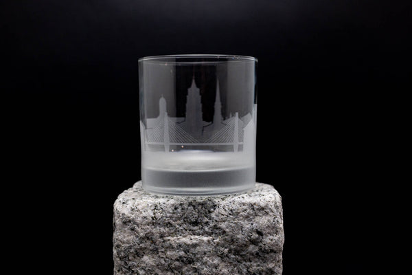 A frosted glass with an etched image of a city skyline on it, placed on a stone pedestal against a black background.