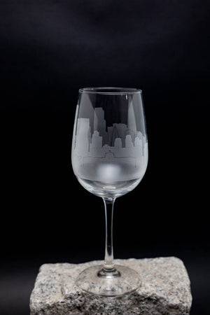 A wine glass with an etched cityscape design on it, placed on a rock against a dark background.