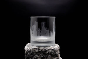 A frosted glass with a city skyline etched onto it, placed on a rock against a dark background.