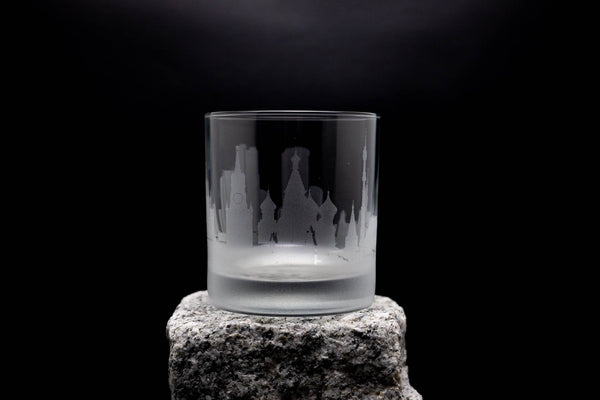 A frosted glass with a city skyline etched onto it, placed on a rock against a dark background.