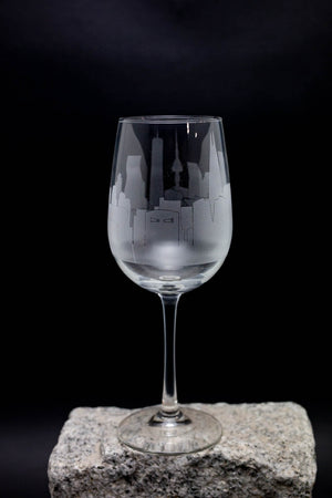 A wine glass with an etched cityscape design on the front, placed on a rock against a dark background.