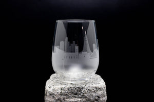 A frosted glass with a city skyline etched onto it, placed on a rock.