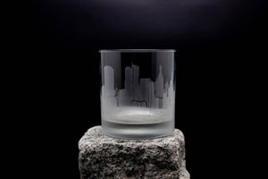 A frosted glass with a city skyline etched on it, placed on a rock against a dark background.